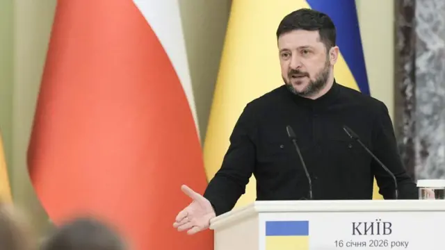 Volodymyr Zelensky speaking behind a podium with microphones on it, wearing black.