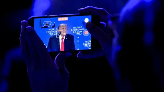 A person in the audience using a mobile phone records a video as US President Donald Trump speaks during his special address at the 56th annual meeting of the World Economic Forum (WEF) in Davos, Switzerland, 21 January 2026
