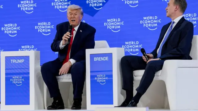 Donald Trump sits next to CEO of the World Economic Forum Borge Brende on white chairs onstage, in front of a blue background.