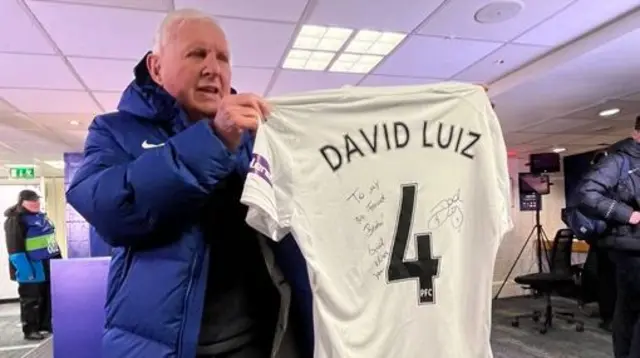 Brian Pullman holding up a David Luiz shirt
