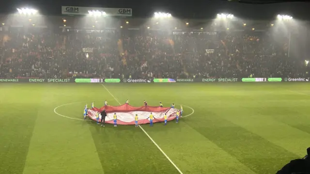 Mascots hold a banner on the centre circle at the LNER Stadium