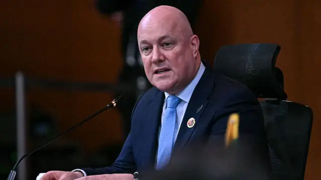 Luxon speaks into a microphone while wearing a suit