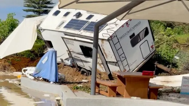 A caravan damaged and lying tilted by a pool