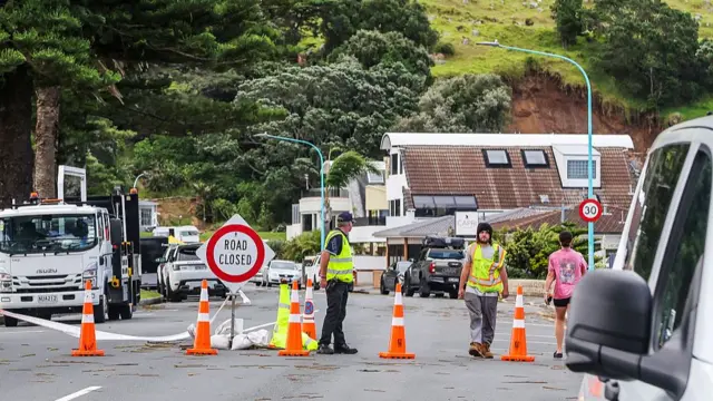 People with neon yellow vests standing beside a "Road Closed" sign