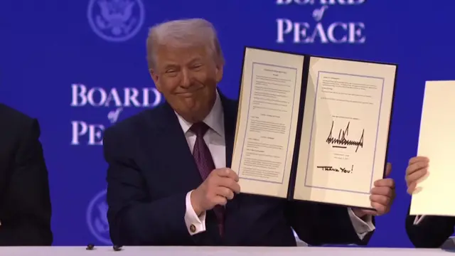 Donald Trump holds up a signed document at the Board of Peace meeting