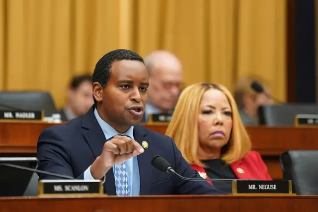 Rep Joe Neguse sits at a microphone in a committee hearing room on Capitol Hill