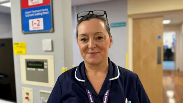 Charlotte Morley, lead practitioner wearing blue nursing uniform while stood on ward