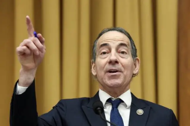 Jamie Raskin points as he speaks in front of a yellow curtain