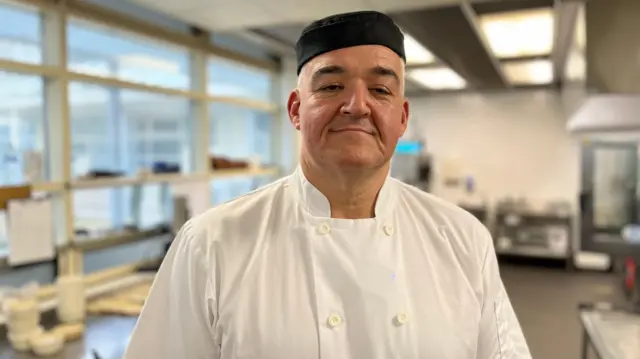 René Bisson is in chef's whites and a black hat in a kitchen.