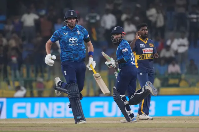 Adil Rashid (C) and Jamie Overton (L) of England takes a single