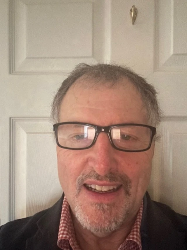 Plymouth doctor Richard Ayres stood in front of white door. He is wearing glasses and a navy top