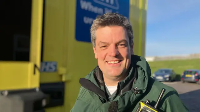 James Atkinson stood in front of an ambulance and smiling at the camera.