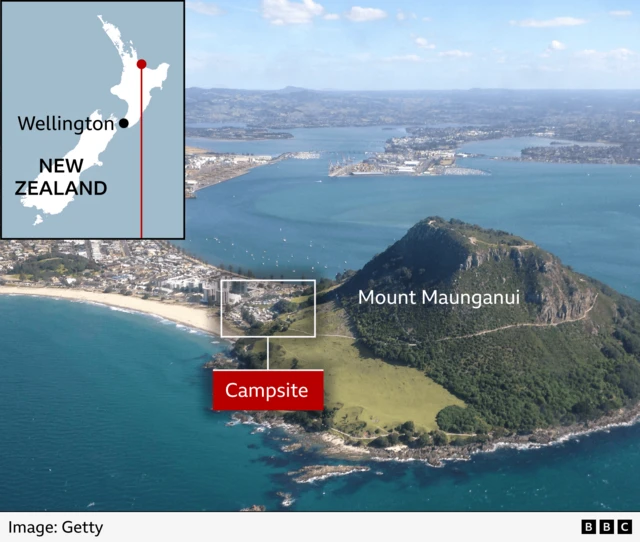 Aerial photograph of Mount Maunganui on New Zealand’s North Island, showing a coastal headland surrounded by blue water, beaches, and a built‑up area. A labelled box marks the location of a campsite near the shoreline. An inset map shows New Zealand with a marker indicating Wellington