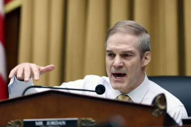 Congressman Jim Jordan gesticulates while speaking into a microphone in front of a yellow curtain