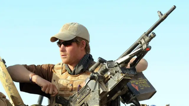 Prince Harry next to a gun attached to a tank