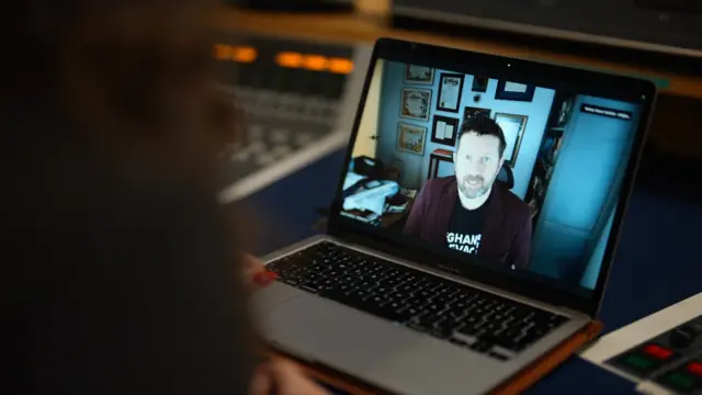 A picture showing an open laptop screen. Shawn is on the screen on a video call and smiles while sitting on a chair.