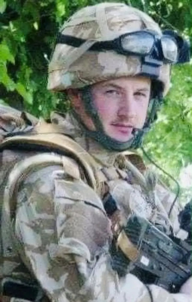 Headshot of Sean in his military uniform holding a gun and looking at the camera. It's quite blurry