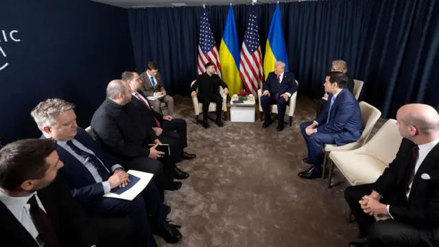 A wide shot of the US-Ukraine negotiation room with officials in chairs in a U-shape