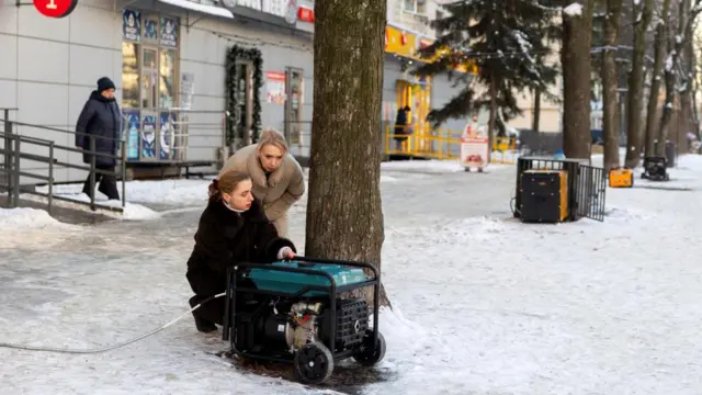 Two women operate a generator on the snow covered ground outside a shop in Kyiv.