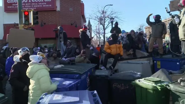 People bang bins with their hands, some sitting and stand on bins, during protest in Minneapolis