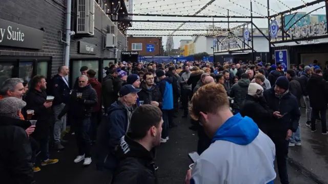 A large group of mostly men drinking beer. They are at a football game.