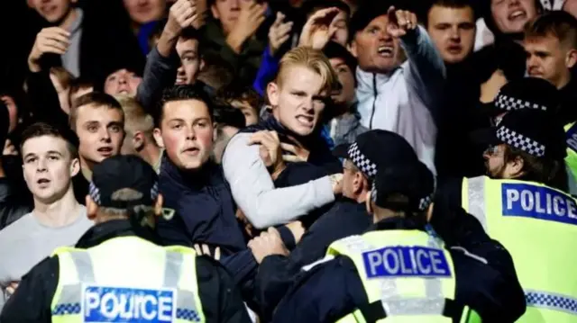 A group of football fans are held back by police.