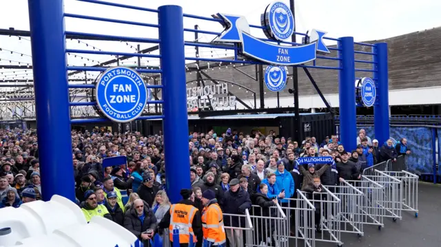 A large crowd of football fans in blue. They are held back behind a gate.