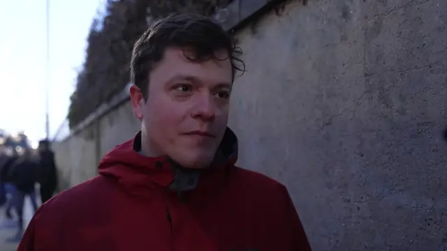 A man in a red jacket. He is talking to a journalist.