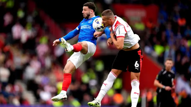 Two football players jostle mid air for a ball.