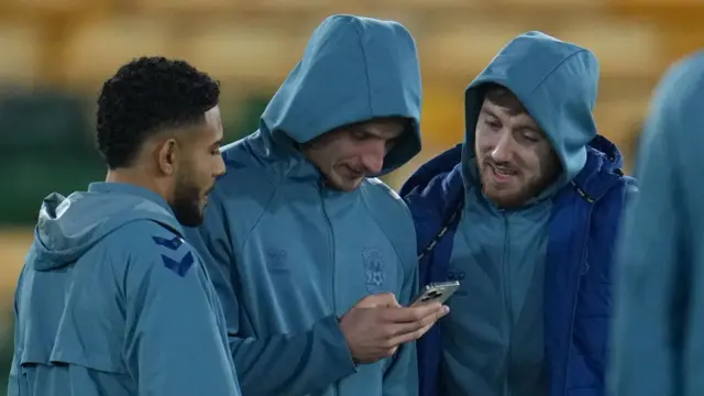 Coventry players check their phones while inspecting the Carrow Road pitch
