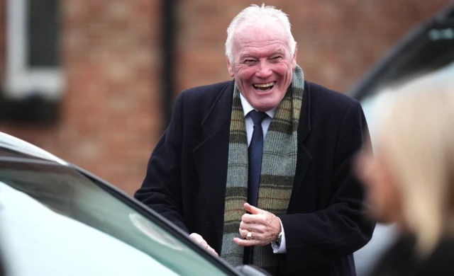 Eddie Gray getting a car smiling. He is wearing a navy suit and jacket with a tartan scarf.
