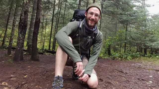 Alex Pretti wears hiking gear and poses for a photo in a wooded area.