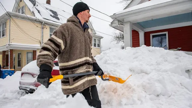 A man with a spade shovelling snow outside a house