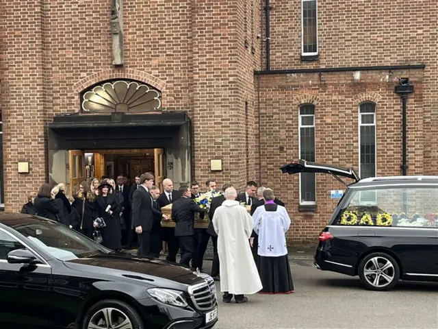 Wide image showing Yorath's coffin being carried into the back hearse.