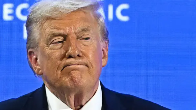 Close up of Trump on stage in front of blue screen wearing navy suit