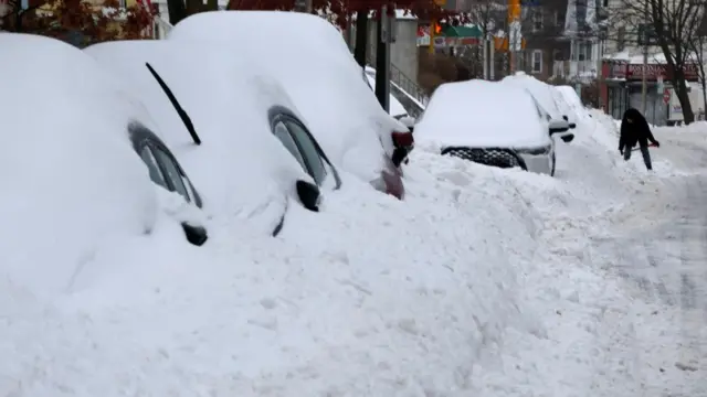 Cars covered in snow. In the background, a person clears the snow away from their car