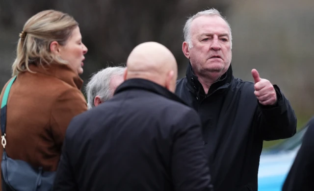 Kevin Ratcliffe among mourners outside the church. He is holding his thumb up.