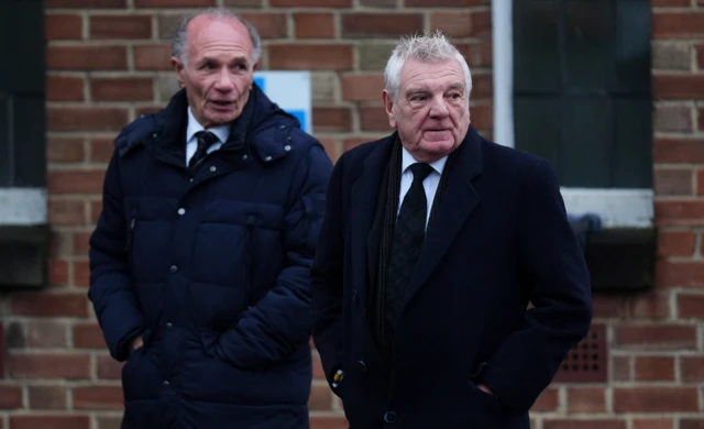 Paul Reaney and Stix Lockwood arriving at the church, both wearing black suits and jackets. Paul is standing on the left.
