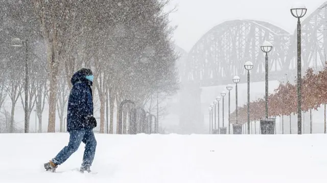 A person walks through snow a few inches deep, as more snow falls