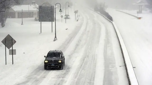 A car drives along an empty road covered in snow and ice