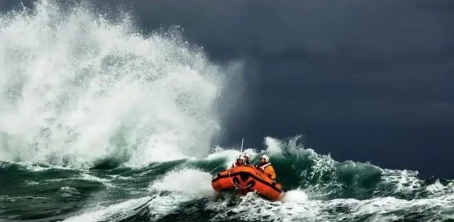 A orange lifeboat and crew crossing fierce waves