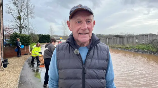 Ed Fisher standing in front of a muddy river with people cleaning up behind him