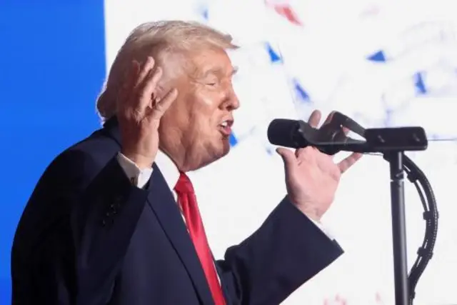 President Donald Trump raises his hands while speaking into a microphone