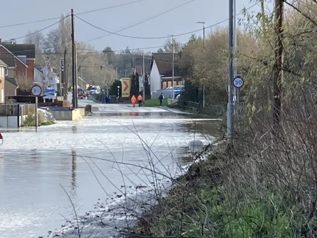 A flooded road in Ilminster, Somerset. In the backgrounf there are houses, along with 30mph signs which are partially under water