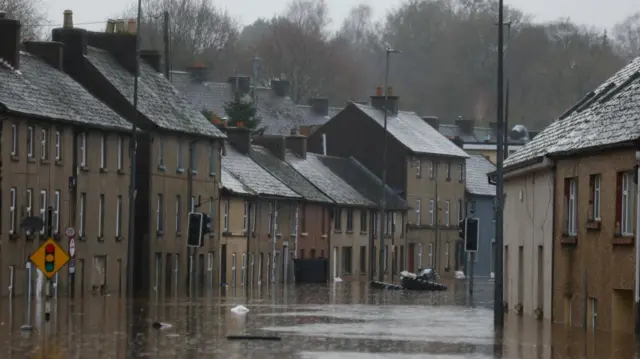 Flood waters fill a street up to people's windows on the ground floor