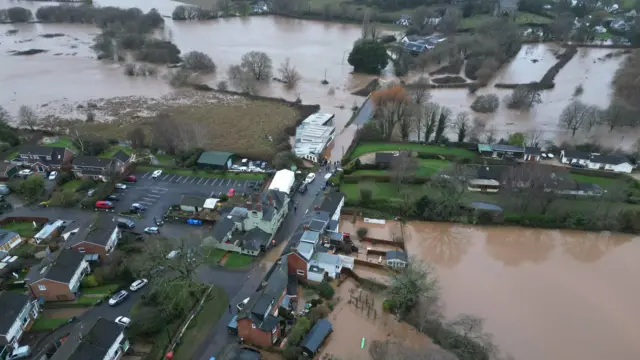 A car park and houses. Around them are large amounts of flood water.
