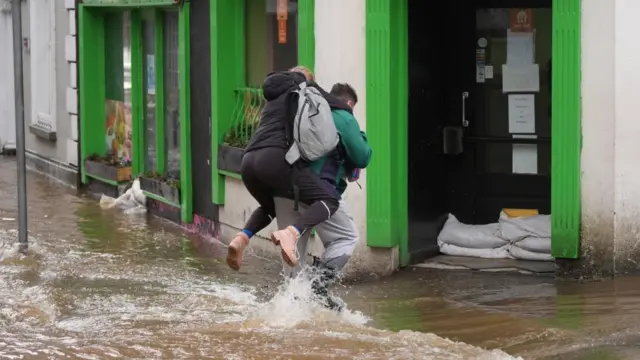 A person carries another person on their back through the flood water in a street