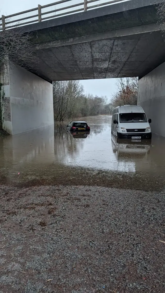 Flooding at Ashurst Bridge Road under A326. Twi vehicles are seen driving through.