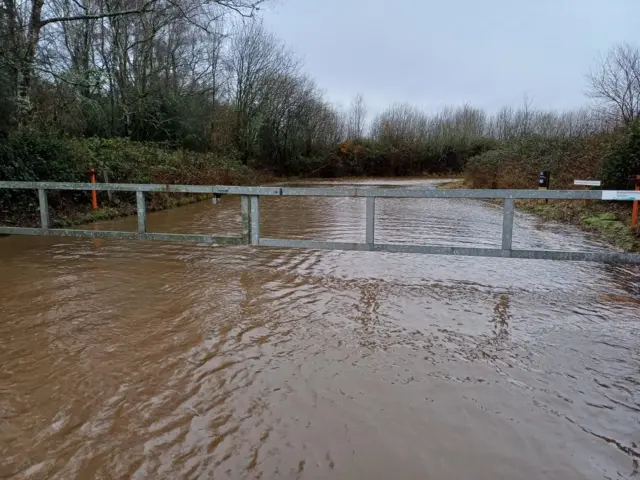 A view of the flooded grounds of Blashford Lakes Nature Reserve and Education Centre. The water level is almost touching a vehicle barrier.