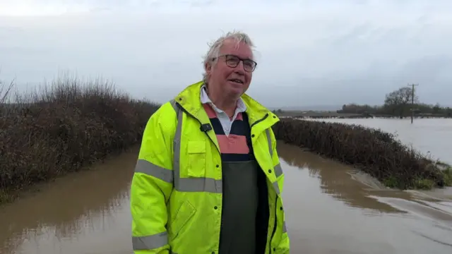 Alan Wilson stood in floodwater outside his home. He is wearing hi-vis.